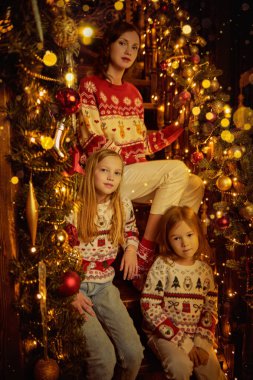 Güzel anne ve tatlı kızları Noel akşamını sıcak bir aile ortamında ışıldayan ışıkların arasında neşeli bir şekilde dekore edilmiş bir merdivende oturarak geçirirler. Mutlu Noeller aile.. 