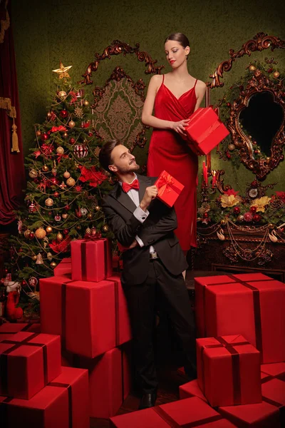 Tatil indirimi ve alışveriş. Lüks gece elbiseleri içinde yakışıklı bir adam ve güzel bir kız Noel arifesinde kırmızı hediye kutularının arasında hediyelerini değiş tokuş ederler. Noel ve Yeni Yıl modası. 