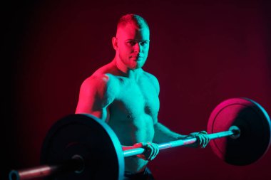 Yakışıklı bir erkek halterci, koyu renkli bir stüdyo arka planında kırmızı ışıklı bir halterle egzersiz yapar. Profesyonel spor. Ağırlık kaldırma. 