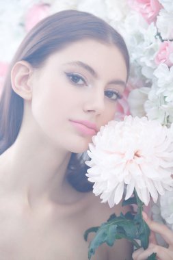 Beauty concept. A beautiful gentle girl stands with a chrysanthemum flower against a wall with delicate white and pink flowers, surrounded by a light haze. Make-up and cosmetics. Perfumery.