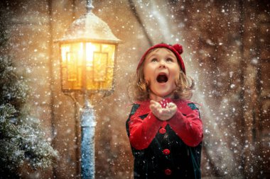 Kış Noel Masalı. Küçük sevimli bir elf kızı kar taneleri yakalar ve sevinir, bir ahşap kulübede durur ve kar yağışının altında karla kaplı bir fener.. 