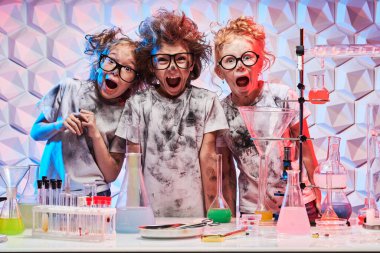 Group of kids with glasses and matted hair scream joyfully in a chemical laboratory after boom from an unsuccessful experiment. Science experiments and children. 