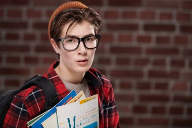 Okul ve eğitim. Modern bir gencin portresi, günlük kıyafetler ve gözlüklerle çalışmaktan ve sınavlardan yorgun düşmüştü. Kopyalama alanı olan tuğla duvar arkaplanı. 