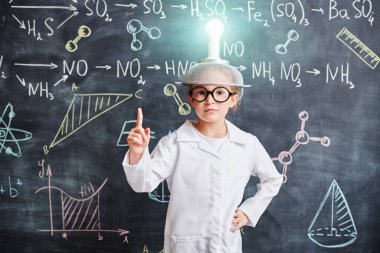 Yeni fikirler ve keşifler. Akıllı bir bilim adamı kız, elinde kimyasal formüllerle kafasında ampul olan bir şapkayla tahtada duruyor ve işaret parmağını kaldırıyor. Evreka! Eğitim. 