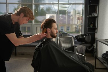 Saç kesimini mükemmel gösteriyor. Yakışıklı esmer adam berber dükkanını ziyaret ediyor. Yan plan çekimi.