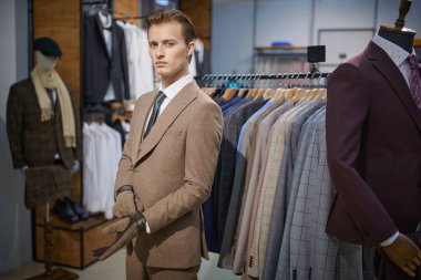 Erkek giyim mağazasında eldiven deneyen yakışıklı, kahverengi takım elbiseli sarışın bir adamın portresi. Erkeklerin iş modası.