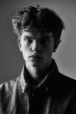 Deri ceketli yakışıklı bir gencin stüdyo portresi. Siyah ve beyaz atış. Erkeklerin gençlik modası. 