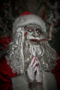 Noel ve Cadılar Bayramı. Korkunç yaşlı, zombi Noel Baba puro içiyor ve karanlık bir Noel odasında dikilirken ellerini kızgın bir şekilde ovuyor..