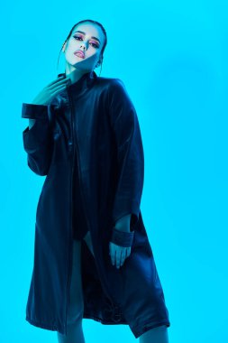 Çekici esmer bir modelin stüdyo portresi. Yüzüne ışık demeti düşmüş mavi bir arka planda siyah deri bir ceketle poz veriyor. Moda fotoğrafı.. 