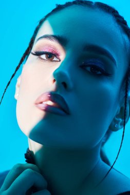 Işık ve gölge arasında parlak makyajlı çekici esmer model. Açık mavi bir arkaplanda stüdyo çekimi. Makyaj ve makyaj malzemeleri. Portreyi kapat.