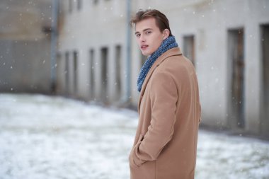 Şık bir kışlık ceketi ve atkısı olan yakışıklı genç bir adam şehir sokaklarında yürüyor. Soğuk kış günü. Erkek modası ve yaşam tarzı.