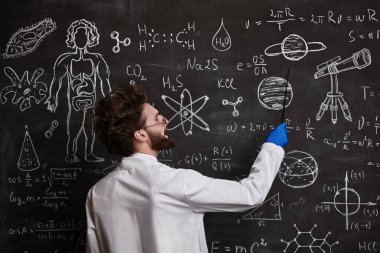 Zeki, hevesli bir bilim adamı tahtaya oturmuş bilimsel formülleri ve şemaları açıklıyor. Bilim ve eğitim.