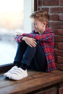 Ekose gömlekli ve kotlu şık, tasasız bir çocuk pencere eşiğine yaslanmış pencereden dışarı bakıp gülümsüyor. Çocuklar ve çocukluk. 