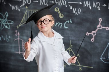 Zeki çocuklar. Beyaz gömlekli ve gözlüklü şirin bir kızın portresi. Elinde öğretmen iğnesi ve kimyasal formüllerle tahtada duruyor. Eğitim. 