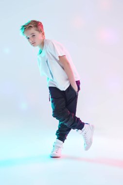 Beyaz tişörtlü, eşofmanlı ve spor ayakkabılı modern yakışıklı break dansçı beyaz arka planda stüdyoda poz veriyor. Tam boy portre. Çocuk modası. Spor ve aktiviteler.