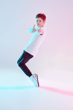 Çağdaş danslar. Profesyonel hip hop ve break dansçı çocuk stüdyoda beyaz arka planda karışık renkli ışıkta dans ediyor. Tam boy portre. 