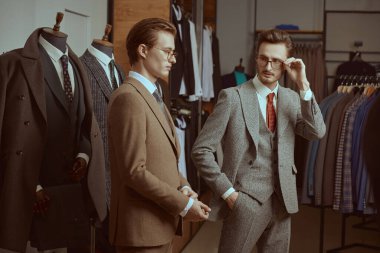 Zarif klasik takım elbiseli ve gözlüklü iki saygıdeğer adam prim erkek giyim mağazasında yan yana durur. İş stili. Erkek modası. 