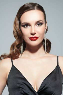 Akşam stili. Parlak makyajlı ve zarif saç stili olan güzel bir bayan model gri bir stüdyo arka planında siyah kadınsı bir gece elbisesiyle poz veriyor. Güzellik ve moda çekimi.. 