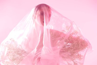 Kozmetik ve parfüm. Şeffaf organzayla kaplı zarif bir kız pembe arka planda narin pembe bir ışıkta duran küçük beyaz çiçekleri elinde tutuyor. Deri ve vücut bakımı.