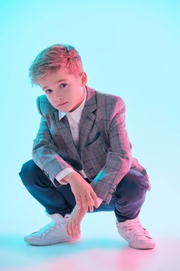 Zekice bir gündelik tarz. Pembe ışıkta açık mavi arka planda şık bir takım elbise, kot pantolon ve spor ayakkabı giymiş yakışıklı bir çocuğun tam boy çekimi. Eğitim. Stüdyo moda çekimi. 