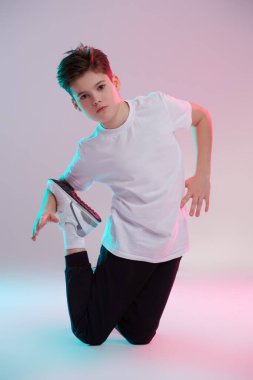 Çocuklar için spor ve aktiviteler. Yakışıklı bir erkek break dansçının beyaz bir arka planda karışık renkli ışıklandırmada günlük spor kıyafetlerinde poz verirken uzun bir çekim. Çocukların spor modası..