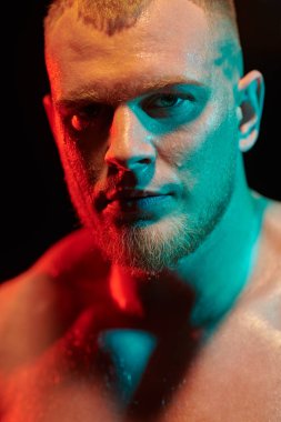 Çok renkli ışıklandırmada siyah bir arka planda yüzü ter içinde kalmış güçlü kızıl saçlı bir atletik adamın portresini yakından çek. Erkek güzellik konsepti.