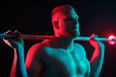 Yakışıklı bir erkek halterci, koyu renkli bir stüdyo arka planında kırmızı ışıklı bir halterle egzersiz yapar. Profesyonel spor. Ağırlık kaldırma. 