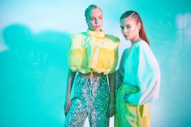 Kıyafet içinde moda yaz renkleri. İki manken yaz koleksiyonundan şık kıyafetler giyip poz veriyor. Moda modası. Aquamarine ışığında stüdyo portresi. 