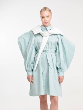 Zarif bir yaz tarzı. Şık, açık mavi bir elbise ve beyaz bir eşarpla poz veren sarışın güzel bir kızın portresi. Beyaz arkaplan. 