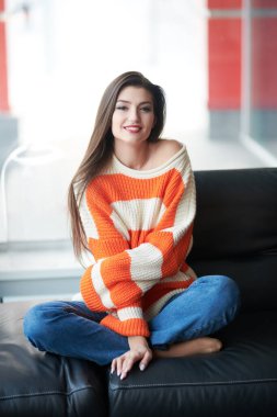 Oturma odasındaki deri koltukta oturan güzel, gülümseyen genç bir kadının portresi. Mutlu hayat, mutlu insanlar konsepti. 