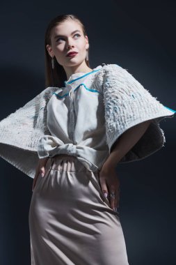 Moda modası. Muhteşem genç kadın manken geniş kollu ve bej düz etekli abartılı bej bluzla poz veriyor. Siyah bir arkaplanda stüdyo resmi.