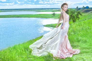 Göz kamaştırıcı, soluk pembe elbiseli, güzel manzaralı, vahşi bir nehir kıyısında duran bir gelinin uzun bir resmi. Düğün stili ve moda. 