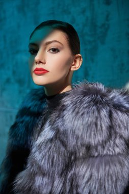 Parlak makyajlı, çekici, zarif bir kız, parlak arka plan ışığı ve gölgesinde muhteşem gümüş bir tilki kürkünün içinde poz veriyor. Moda fotoğrafı. Lüks stil.