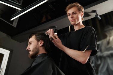 Berber dükkanında müşteriye hizmet eden kuaför. Yakışıklı esmer adam kuaför salonunu ziyaret ediyor..