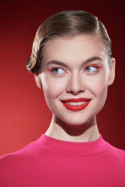 Parlak kırmızı rujlu güzel bir sarışın kız ve kırmızı arka planda büyüleyici bir şekilde gülümseyen kırmızı okları var. Makyaj ve makyaj malzemeleri. Güzellik konsepti.