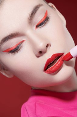 Sevimli kırmızı renk. Gözlerinde parlak kırmızı oklar ve kırmızı bir arka planda muhteşem kırmızı ruj olan güzel bir kız modelin portresi. Makyaj ve makyaj malzemeleri. Yakın çekim..