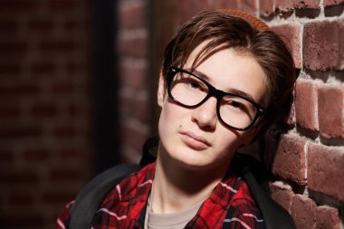 Yakışıklı, modern, gözlüklü bir gencin portresi, şık, sıradan kıyafetler ve duvara yaslanmış bir şapka. Ergenler ve duygular. Gençlik modası. Yakın çekim.. 
