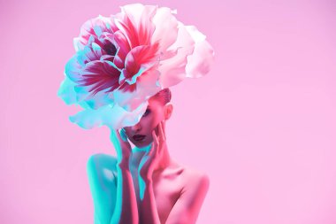 Kadın güzelliği ve çiçekler. Zarif çıplak bir kadının portresi güzel büyük bir şakayık çiçeğiyle poz vererek yüzünü pembe bir arka planda gizliyor. Deri ve vücut bakımı, kozmetik ürünleri. 