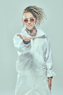 Rastalı ve güneş gözlüklü şık bir punk rock müzisyeni sevinçle gülümseyip elini uzatıyor. Gençlik alternatif kültürü. Beyaz stüdyo geçmişi. 