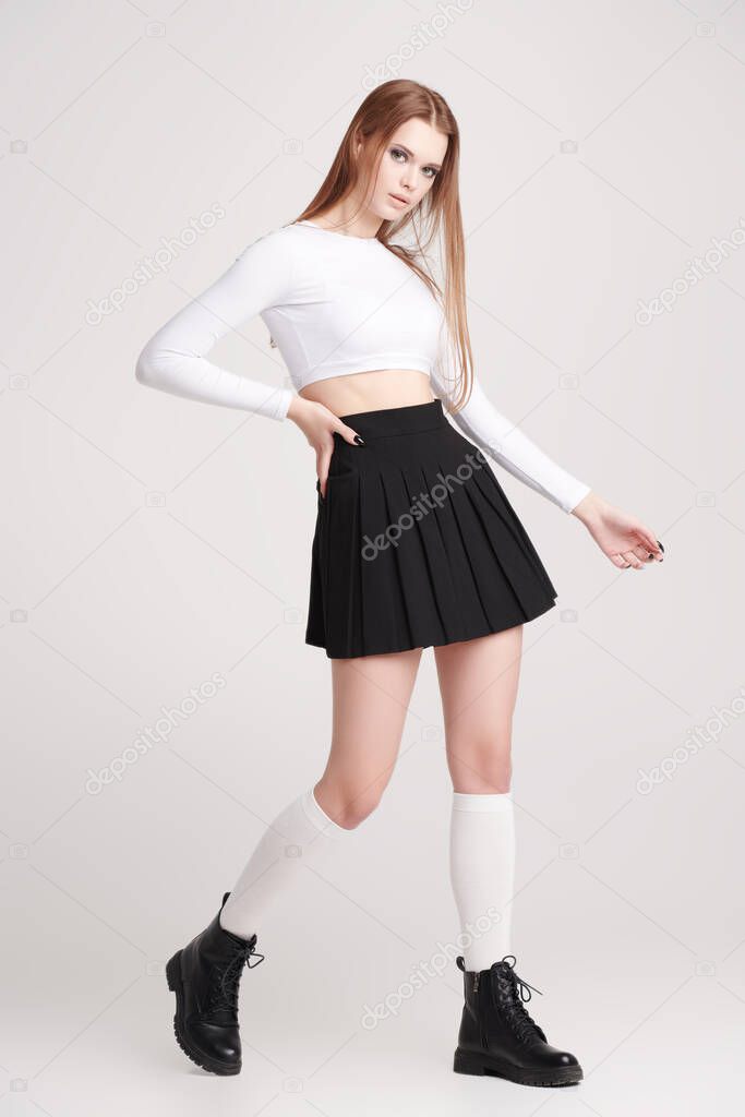 Portrait of a cool, sexy girl in a trendy white top and black school skirt  posing at the studio on a white background. Modern youth dances. 