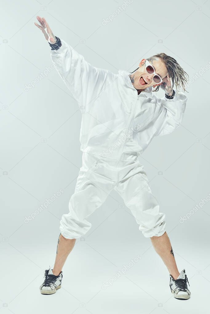 Modern stylish punk rock musician with dreadlocks in white suit and white sunglasses singing joyfully on a white background. Youth alternative culture. Futuristic space and cybepunk style. 