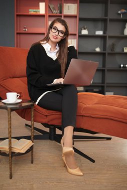 Güzel bir iş kadını, modern bir ofiste bir koltukta dizüstü bilgisayarla çalışıyor. İş ve iletişim. Modern iç mekan, mobilya.