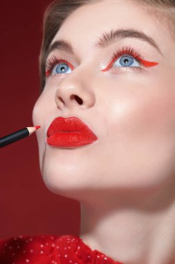 Makyaj ve makyaj malzemeleri. Parlak kırmızı rujlu güzel bir kız modelin portresi dudaklarını kaplamak için kırmızı bir dudak kalemi sürüyor. Yakın çekim..