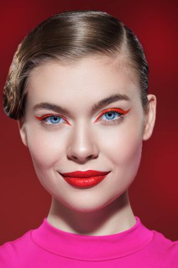 Güzellik konsepti. Parlak kırmızı rujlu güzel bir sarışın kız ve kırmızı arka planda büyüleyici bir şekilde gülümseyen kırmızı okları var. Makyaj ve kozmetik. 