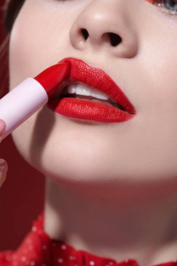 Sevimli kırmızı renk. Güzel bir kız modelin parlak kırmızı ruj sürerken çekilmiş bir fotoğrafı. Yakın çekim. Makyaj ve kozmetik. 