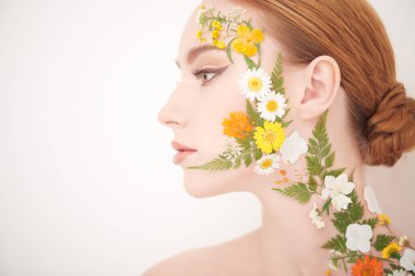Zarif makyajlı ve yüzünde yaz çiçekleri olan güzel, genç bir kadının portresi. Kopyalama alanı olan beyaz arkaplan. Parfüm. Çiçek kokuları. Makyaj ve kozmetik. 
