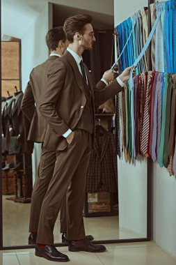 Zarif klasik takım elbiseli ve gözlüklü saygıdeğer bir işadamı kaliteli erkek giyim mağazasından uygun kravatlar seçiyor. Erkek modası, iş tarzı.. 