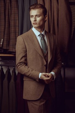 Zarif kahverengi takım elbiseli yakışıklı bir sarışının portresi premium erkek giyim mağazasında duruyor. Erkeklerin iş modası.