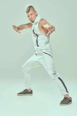 Havalı sarışın punk müzisyeninin portresi Mohawk 'lı ve kollarını kaplayan dövmeli hafif bir stüdyoda poz veren. Siber punk stili. 