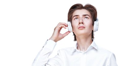 Kafasında kulaklıkla beyaz tişörtlü, kulaklıklı, modern genç bir çocuk kulaklıkla bir şeyler dinliyor ve ciddi ciddi yukarı bakıyor. Ergenler ve eğitim. Beyaz arkaplan. 